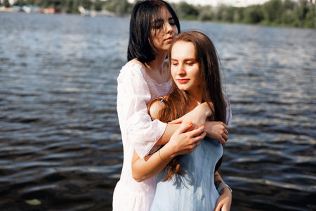 Two teenager girls sitting on a pier at the river bank having a good time in summer. happy girl friends relaxing outdoor near lake.の写真素材