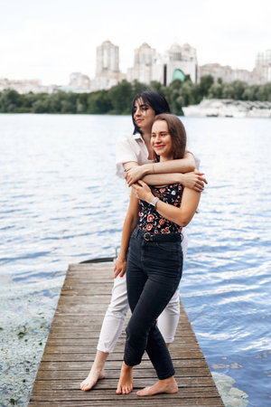 Two beautiful young women standing on the pier and hugging each other.の写真素材