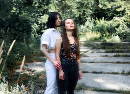 Two beautiful young women in jeans and white blouse walking in the park.の写真素材