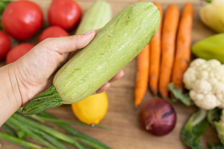 Woman's hand holding zucchini with fresh vegetables on wooden backgroundの写真素材
