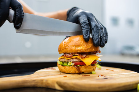 cropped image of woman cutting hamburger with knife on wooden boardの写真素材