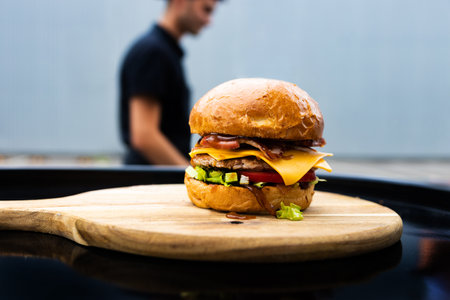 Cheeseburger on a wooden board with a man in the backgroundの写真素材