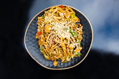 Stir fry udon noodles with pork and colorful vegetables in black platter isolated on white...