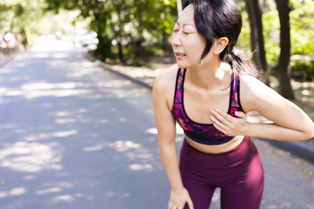 Female asian athlete, has chest pain fitness in the park and running, heart aches after cardio...