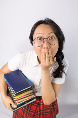 Asian female student holding books and covering her mouth with hand on white backgroundの写真素材