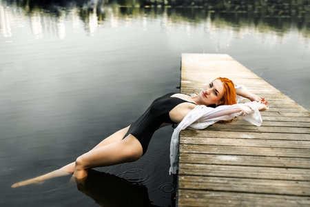 Young redhead woman in a black swimsuit on a wooden pier.の写真素材