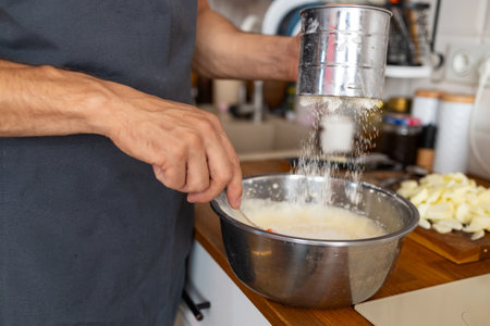 Close-up of a caucasian man in a blue T-shirt kneading dough in a metal bowl
