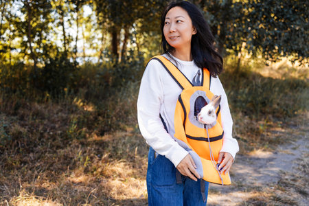 Smiling asian woman holding rabbit in her arms while walking outdoorsの写真素材