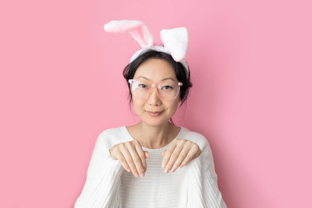 Happy easter day. Asian woman wearing bunny ears on pink backgroundの写真素材
