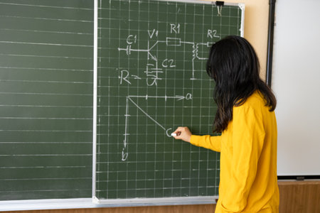 Back view of asian female teacher writing on blackboard in classroomの写真素材