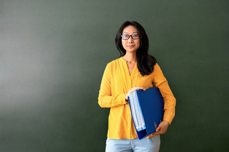 Back to school. Positive asian teacher woman with glasses standing with notebook in school class. Learning education care parenting.の写真素材