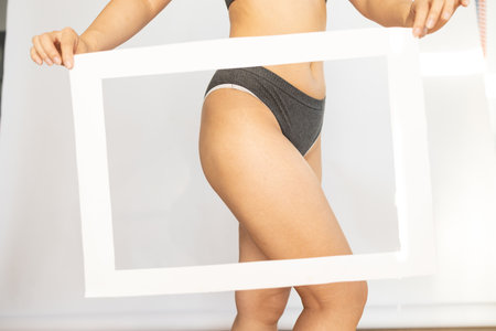 Asian girl holding frame posing in lingerie and having fun. Concept about body positivityの写真素材