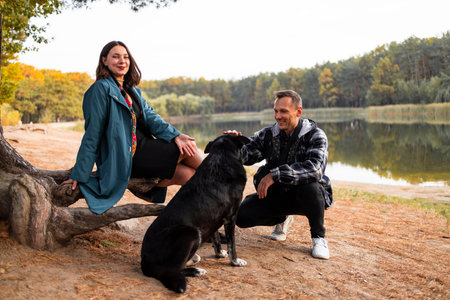 Young couple playing with a dog at the lake in autumn park.の写真素材
