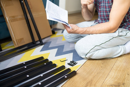 Young man sitting on the floor and reading instructions for assembling furniture at homeの写真素材