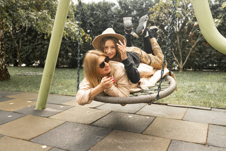 Mother and daughter having fun on a swing in the park. Happy family concept.