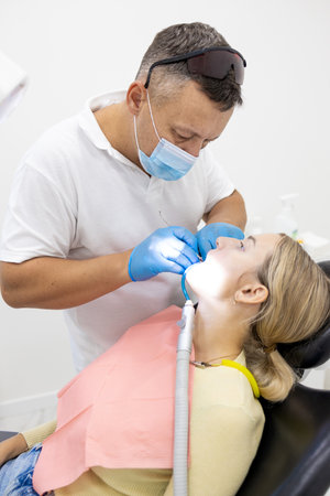 Male dentist treating teeth to young woman patient in clinic. Dental check up.の写真素材