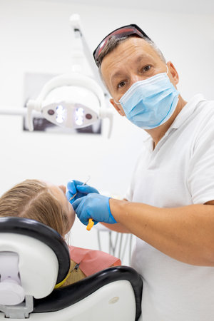 Portrait of male dentist in medical center standing near the chairの写真素材