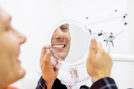 Your smile is our mission. Handsome male patient looking at his beautiful smile sitting at the dental office. Close upの写真素材