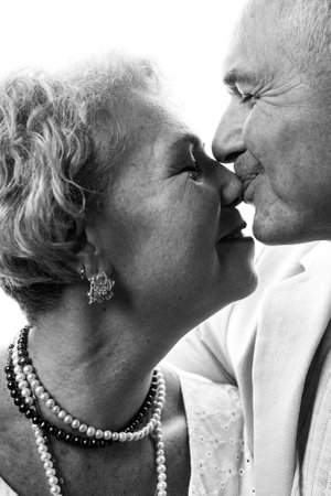 Black and white portrait of a senior couple kissing on a white backgroundの写真素材