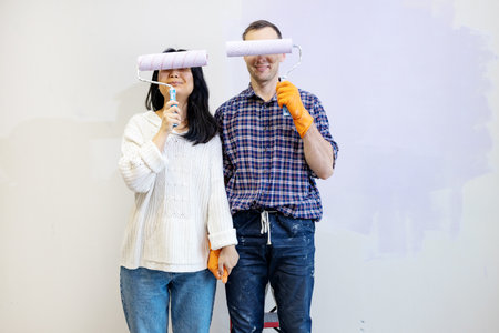 Young couple painting wall in their new house. They are holding paint rollerの写真素材