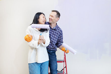 Happy young couple painting interior wall of new house. They are standing on ladderの写真素材