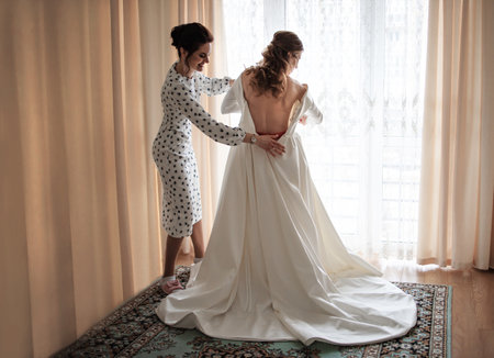 Beautiful bride in white dress and her bridesmaid in a roomの写真素材