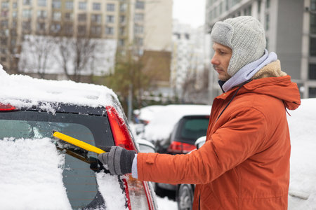 Young Caucasian man cleaning snow from car with brush. Transport, winter, people and vehicle...