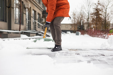A man cleans the snow from the sidewalk with a shovel in winterの写真素材