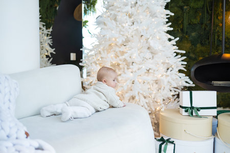 Cute baby boy sitting on the sofa in the room decorated for Christmas