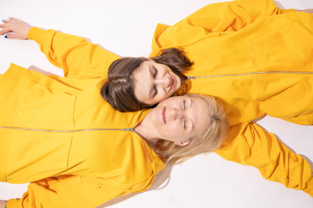 Mother and daughter in yellow overalls lying on the floor, top view