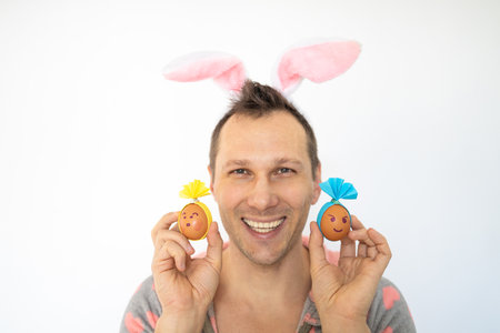 Young man wearing bunny ears and holding easter eggs on white background