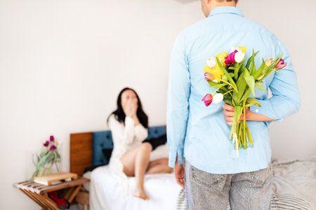 Young man greeting his girlfriend with bouquet of tulips for Valentine's Day at home.の写真素材