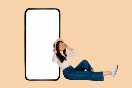 Full body young Asian woman wear straw hat sit near big huge blank screen mobile cell phone with...
