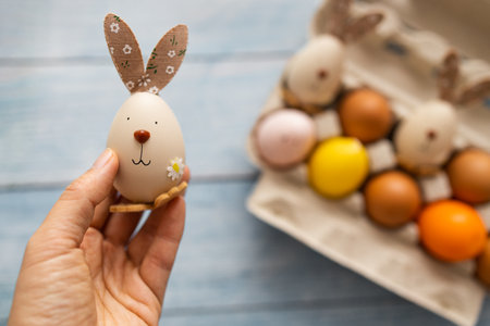 Child hands holding easter egg with funny face and bunny ears. Preparing for Easter, handmade painting concept. Close up, copy space.の写真素材