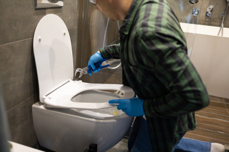Professional plumber working with toilet bowl in bathroom