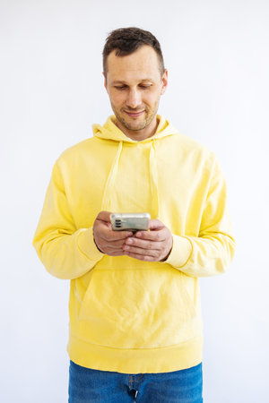 Young man using a mobile phone in a yellow hoodie on a white backgroundの写真素材
