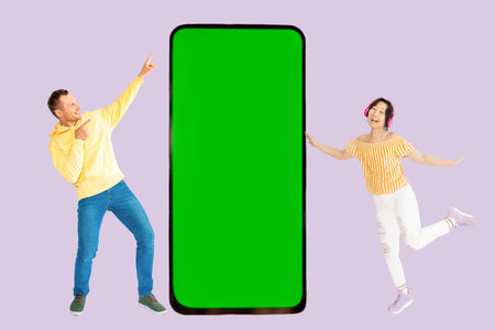 Full length portrait of a young couple jumping with big smartphone with green screenの写真素材