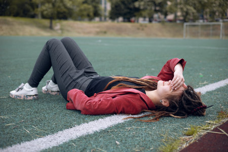 A happy teen girl lies on the grass on the playground. Daytime, stadium, open airの写真素材