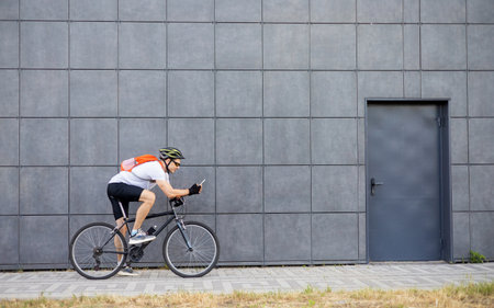 Professional cyclist in sport clothes, helmet and glasses using modern cell phone while sitting on...