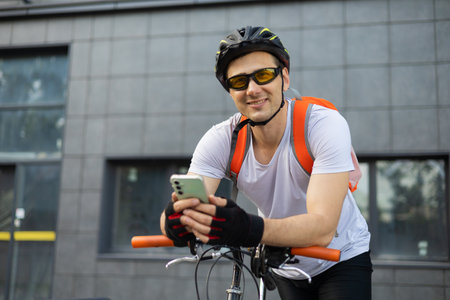 Fit happy cylcist man checking his phone sitting on the city street near the crossing. Relaxed...