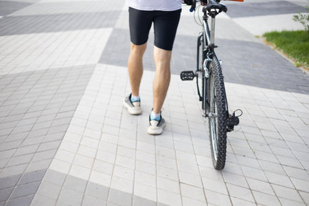 Low section of young man standing with bicycle on sidewalk in the city