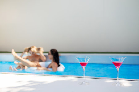 selective focus of cocktail glasses near blurred women in swimming pool at resort