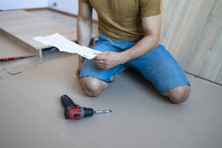 One Caucasian Man Putting Together Self Assembly Furniture at Home holding electric screwdriver looking the instructions - DIY concept real people copy spaceの写真素材