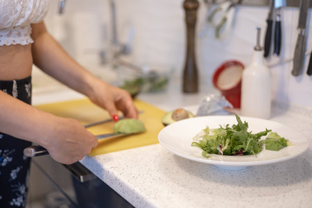 Young adult woman preparing vegetable salad in kitchen. Concept of healthy food, diet and eco food.の写真素材