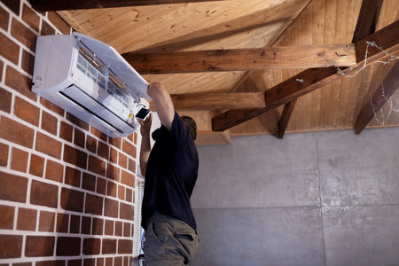 Electrician repairing an air conditioner on a wall in a houseの写真素材