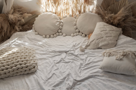 Close up shot of cushions in cotton pillowcases on comfortable bed in cozy bedroom at home. Boho chic interior design in apartment.の写真素材