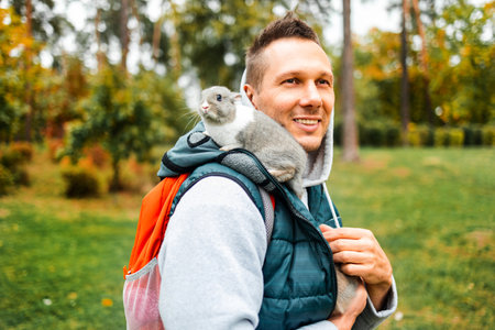 Close portrait of a man with a small rabbit. A gray fluffy bunny sits on shoulder of his owner in...