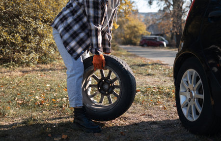 Close-up of a woman changing a car wheel in the autumn parkの写真素材