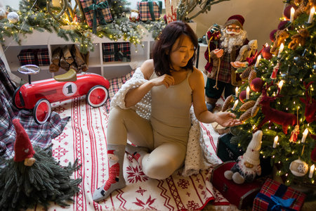Young woman sitting on the floor in front of a decorated Christmas treeの写真素材
