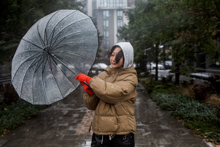 Asian woman trying to hold her umbrella in strong wind and snowfall in winter.